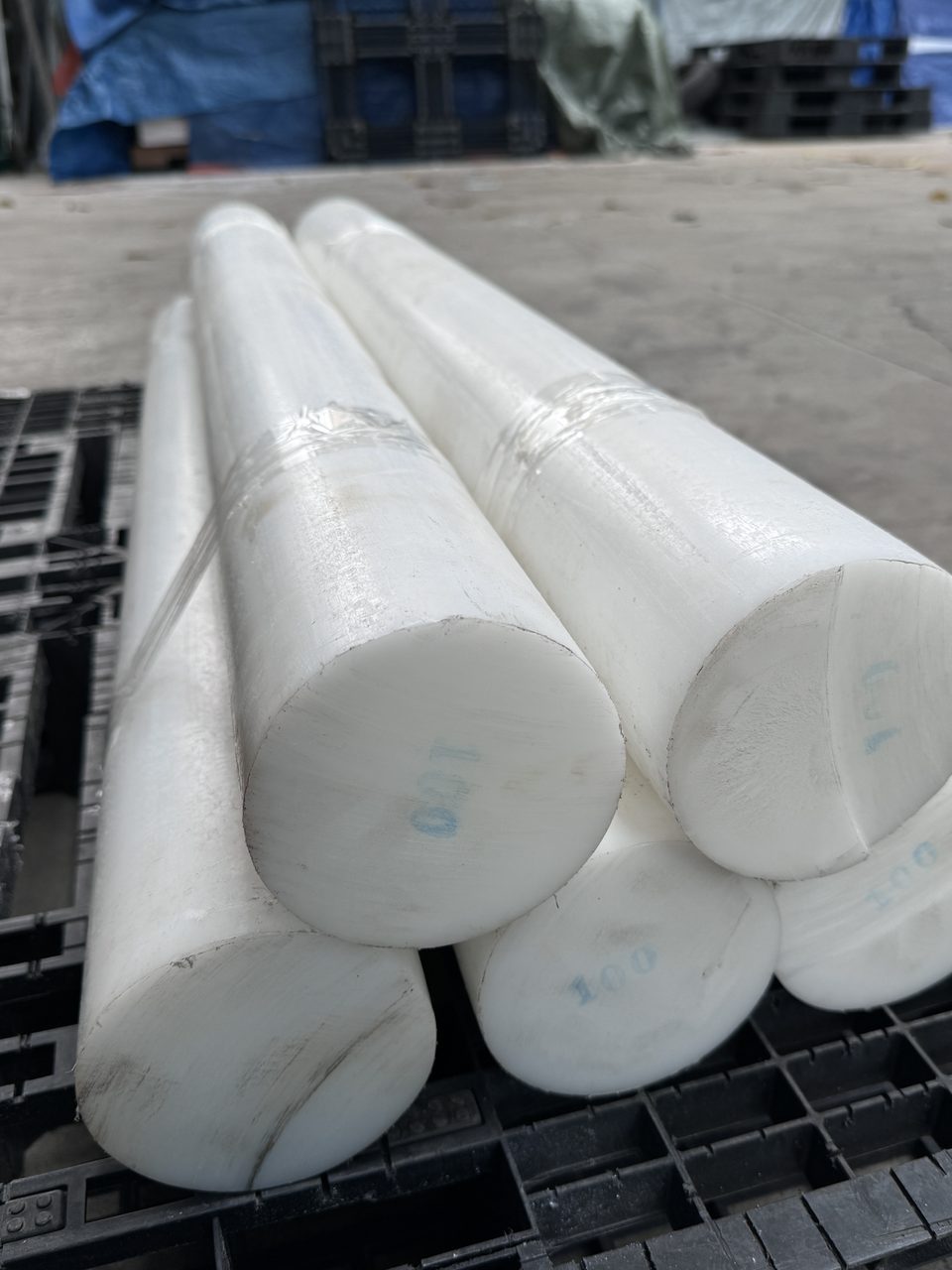 Các cây nhựa POM tròn đặc màu trắng xếp trên pallet nhựa, đầu cây ghi số 100