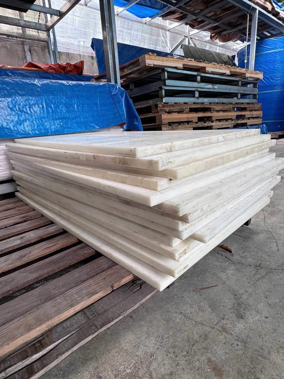 Chồng tấm nhựa POM trắng ngà xếp trên pallet gỗ trong kho