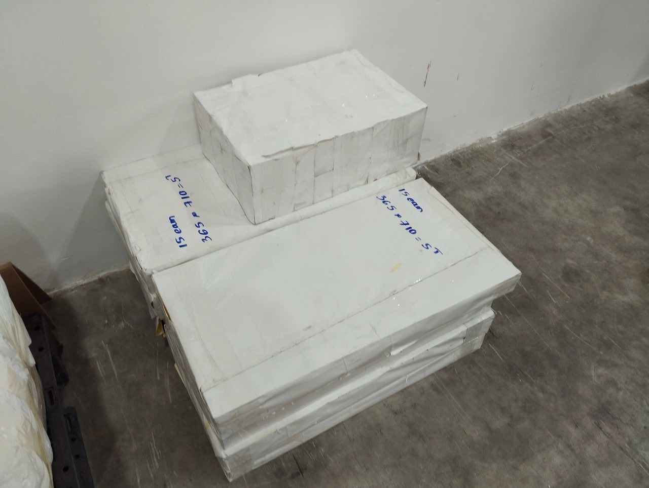 Các kiện nhựa POM cắt sẵn bọc giấy trắng, có ghi chú bằng bút xanh, đặt dưới sàn kho