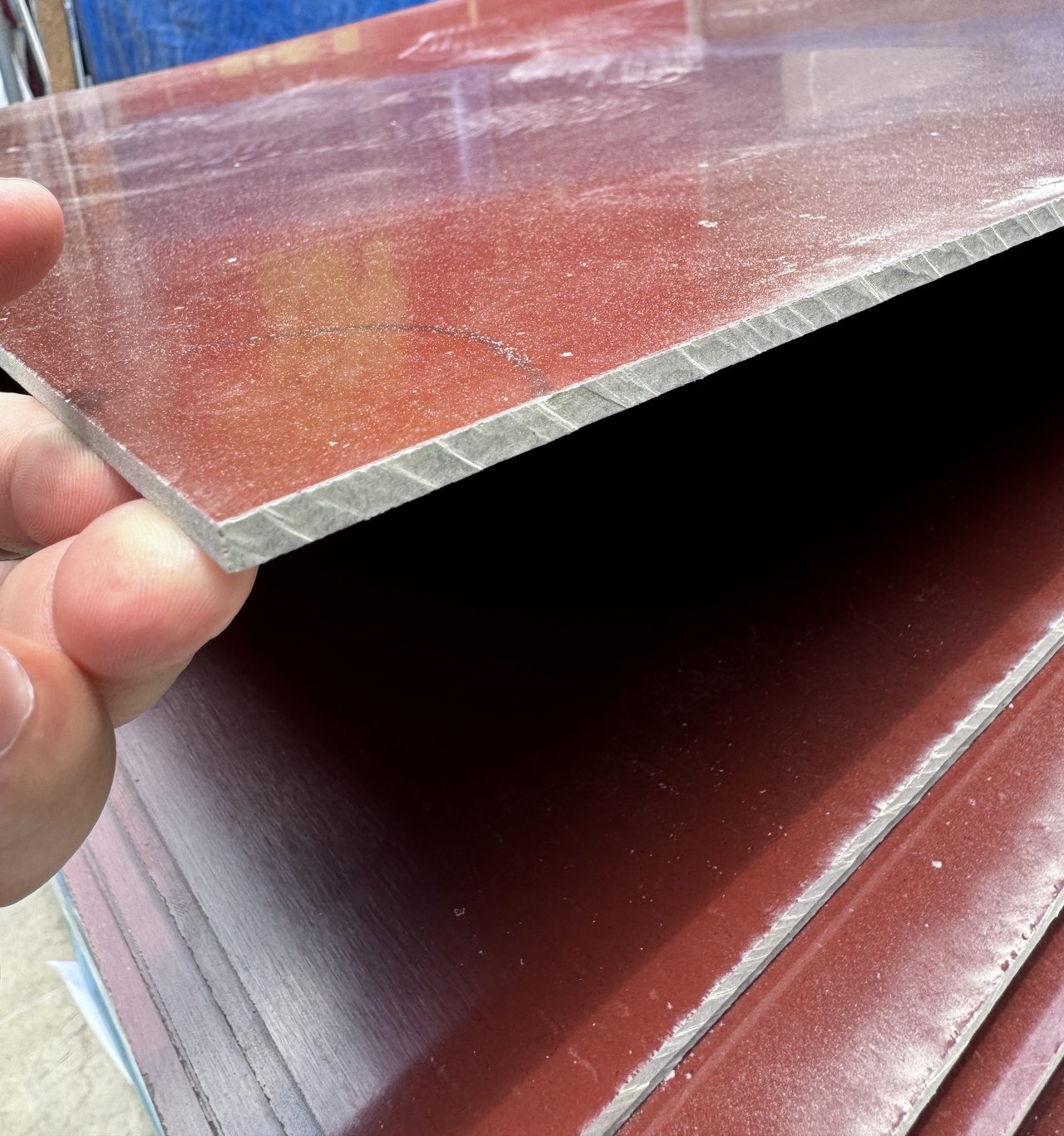 Tay nâng mép một tấm phíp nâu cốt giấy, thấy mép cắt màu xám nhạt